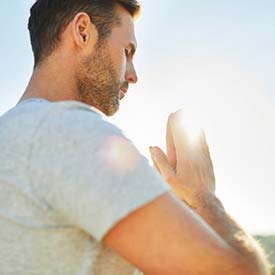 Man sitting with hands together meditating in sunlight after float therapy session