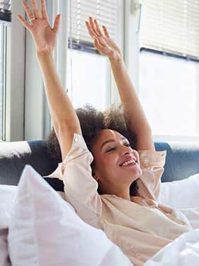 Woman waking up smiling in bed from better sleep after float therapy session with reduced insomnia