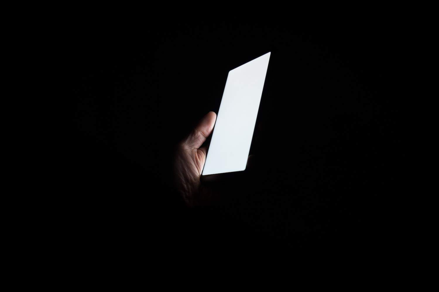 Hand holding up bright smartphone screen in pitch black room after flotation session